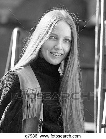 Stock Photograph - 1970s SMILING YOUNG WOMAN WITH STRAIGHT BLOND HAIR PARTED IN MIDDLE WEARING FRINGED LEATHER VEST PORTRAIT LOOKING AT CAMERA. Fotosearch