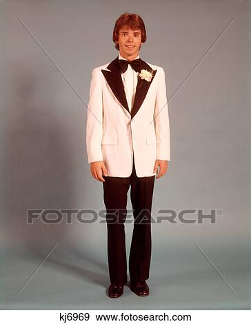 Stock Photo - 1970s TEEN BOY FULL FIGURE PORTRAIT WEARING FORMAL TUXEDO WHITE JACKET FOR PROM DATE STANDING LOOKING AT CAMERA. Fotosearch