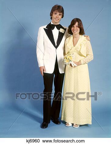 1970s TEEN COUPLE DRESSED FOR PROM GIRL YELLOW LONG DRESS GOWN BOY WHITE TUXEDO BLACK LAPELS STANDING TOGETHER LOOKING AT CAMERA View Large Photo Image Stock Image - 1970s TEEN COUPLE DRESSED FOR PROM GIRL YELLOW LONG DRESS GOWN BOY WHITE TUXEDO BLACK LAPELS STANDING TOGETHER LOOKING AT CAMERA. Fotosearch