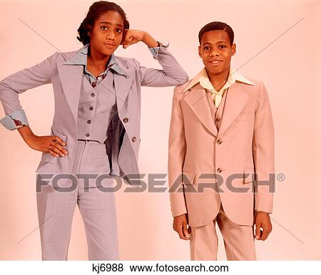 1970s TWO AFRICAN AMERICAN TEENAGERS A BOY IN A BEIGE SUIT AND GIRL IN A BLUE PANTS SUIT STANDING TOGETHER LOOKING AT CAMERA View Large Photo Image Stock Photo - 1970s TWO AFRICAN AMERICAN TEENAGERS A BOY IN A BEIGE SUIT AND GIRL IN A BLUE PANTS SUIT STANDING TOGETHER LOOKING AT CAMERA. Fotosearch