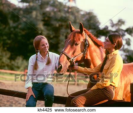 Stock Photography - 1970S Two Teen Girls Sitting Fence Holding Halter Chestnut Horse. Fotosearch