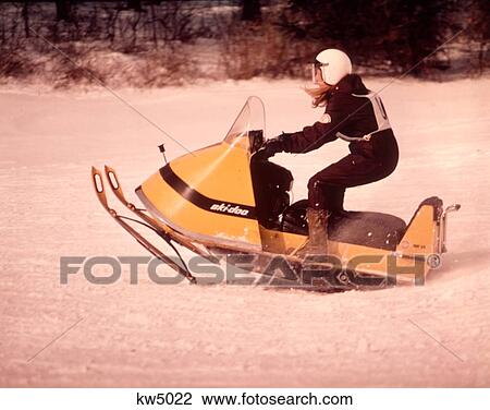 Stock Image - 1970S Woman Driving Yellow Skidoo Snowmobile In Race. Fotosearch