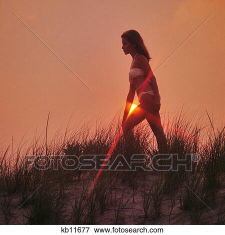 1970s WOMAN SILHOUETTED STANDING ON SAND DUNE SETTING SUN MAKING SUNBURST RAYS AGAINST HER ARM AND THIGH View Large Photo Image Stock Photo - 1970s WOMAN SILHOUETTED STANDING ON SAND DUNE SETTING SUN MAKING SUNBURST RAYS AGAINST HER ARM AND THIGH. Fotosearch