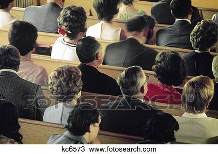 Stock Image - 1980s ADULT MEN AND WOMEN PEOPLE SITTING IN CHURCH PEWS. Fotosearch