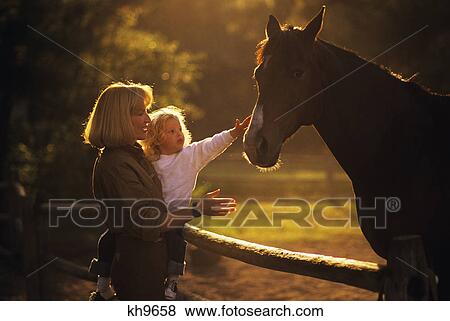 1980s BACKLIT SILHOUETTED BLOND WOMAN MOTHER HOLDING CHILD DAUGHTER REACHING OUT TO TOUCH HORSE View Large Photo Image Stock Photo - 1980s BACKLIT SILHOUETTED BLOND WOMAN MOTHER HOLDING CHILD DAUGHTER REACHING OUT TO TOUCH HORSE. Fotosearch