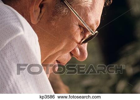 Stock Photograph - 1980s CLOSE-UP PORTRAIT SIDE OF MATURE MAN'S FACE LOOKING DOWN WEARING EYEGLASSES. Fotosearch