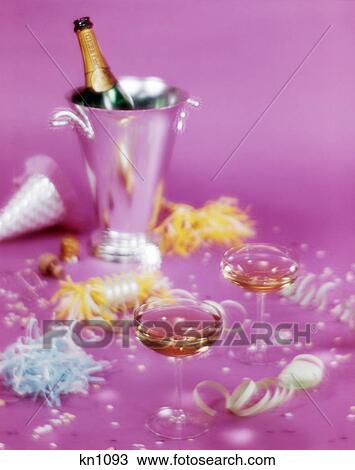 Stock Image - 1980s NEW YEARS EVE STILL LIFE TWO CHAMPAGNE GLASSES ICE BUCKET STREAMERS CONFETTI PINK BACKGROUND. Fotosearch