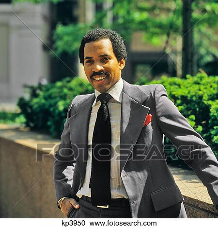 Stock Image - 1980s PORTRAIT SMILING AFRICAN AMERICAN MAN WEARING BUSINESS SUIT AND TIE LOOKING AT CAMERA. Fotosearch