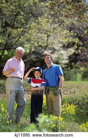 Stock Photography - 1980s THREE GENERATIONS FATHER SON AND GRANDSON STANDING TOGETHER IN FIELD. Fotosearch
