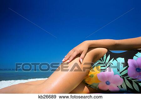 Stock Photo - 1980s WOMAN WEARING FLOWERED ONE PIECE SWIM SUIT FROM CHEST DOWN WAIST HIPS AND THIGHS MANICURED HAND ON HIP LYING ON BEACH. Fotosearch