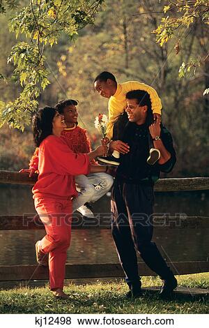 1990s AFRICAN AMERICAN FAMILY STANDING BY FENCE IN AUTUMN BOY HANDING FLOWERS TO MOTHER View Large Photo Image Stock Photo - 1990s AFRICAN AMERICAN FAMILY STANDING BY FENCE IN AUTUMN BOY HANDING FLOWERS TO MOTHER. Fotosearch