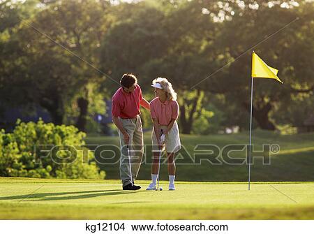 Picture - 1990s MAN TEACHING WOMAN TO PLAY GOLF STANDING ON PUTTING GREEN. Fotosearch