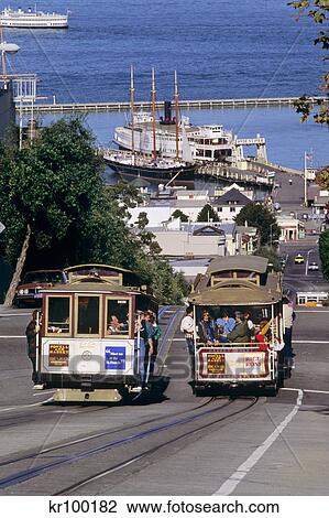 Stock Image - 1990s TWO CABLE CARS ON HYDE STREET SAN FRANCISCO MARITIME NATIONAL HISTORICAL PARK IN DISTANCE SAN FRANCISCO CALIFORNIA USA. Fotosearch