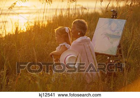 1990s WOMAN ARTIST PAINTER AND GRANDDAUGHTER WITH CANVAS ON EASEL BY THE BEACH AT SUNSET View Large Photo Image Stock Image - 1990s WOMAN ARTIST PAINTER AND GRANDDAUGHTER WITH CANVAS ON EASEL BY THE BEACH AT SUNSET. Fotosearch