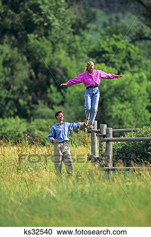 1990s WOMAN WEARING PINK SHIRT WALKING ON TOP OF FENCE MAN WALKING BESIDE THE FENCE SPOTTING HER View Large Photo Image Stock Image - 1990s WOMAN WEARING PINK SHIRT WALKING ON TOP OF FENCE MAN WALKING BESIDE THE FENCE SPOTTING HER. Fotosearch