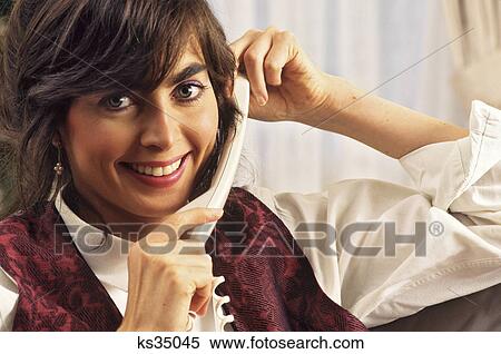 Stock Photography - 1990s YOUNG WOMAN ON TELEPHONELOOKING AT CAMERA SMILING. Fotosearch