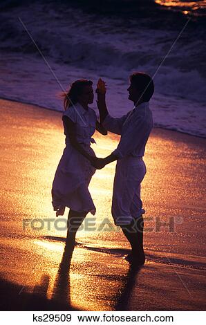 ANONYMOUS SILHOUETTED COUPLE STANDING ON THE BEACH AT WATER'S EDGE AT SUNSET View Large Photo Image Stock Photo - ANONYMOUS SILHOUETTED COUPLE STANDING ON THE BEACH AT WATER'S EDGE AT SUNSET. Fotosearch
