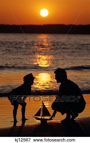 ANONYMOUS SILHOUETTED FATHER AND SON AT THE BEACH WITH TOY SAILBOAT AT SUNSET View Large Photo Image Stock Photo - ANONYMOUS SILHOUETTED FATHER AND SON AT THE BEACH WITH TOY SAILBOAT AT SUNSET. Fotosearch