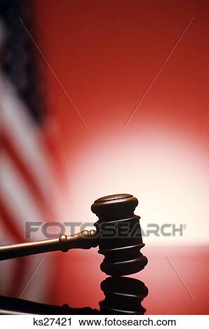 Stock Image - GAVEL RESTING ON REFLECTIVE BENCH SURFACE WITH AMERICAN FLAG IN BACKGROUND. Fotosearch