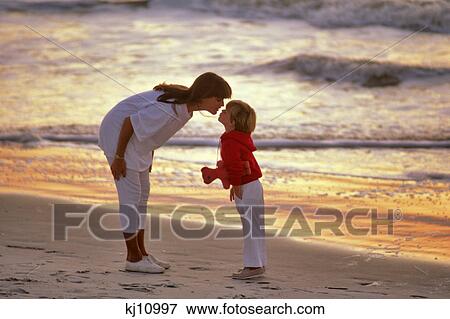 MOTHER BENDING TO KISS SON ON FOREHEAD WHILE WALKING ON BEACH AT SUNSET View Large Photo Image Stock Photo - MOTHER BENDING TO KISS SON ON FOREHEAD WHILE WALKING ON BEACH AT SUNSET. Fotosearch