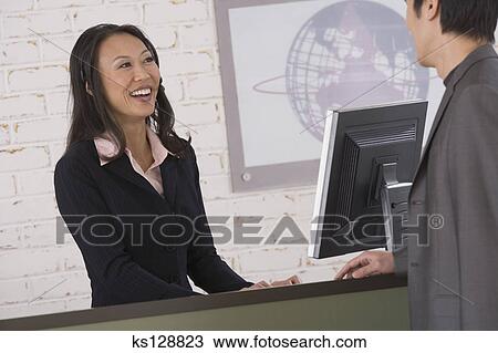 Receptionist Smiling At Businessman From Behind Front Desk Stock