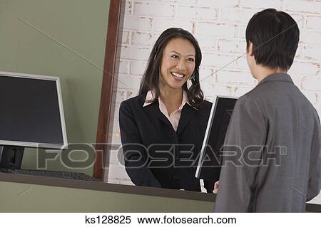 Receptionist Smiling At Businessman From Behind Front Desk Stock