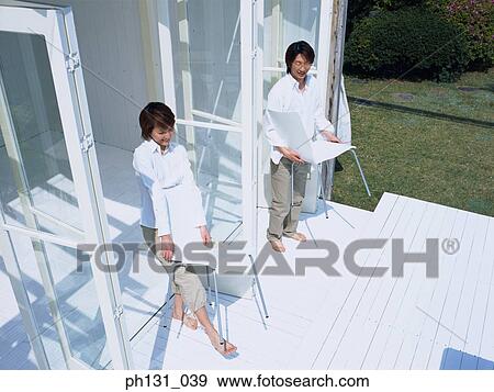 Stock Photo - Asian couple carrying chairs to the porch. Fotosearch