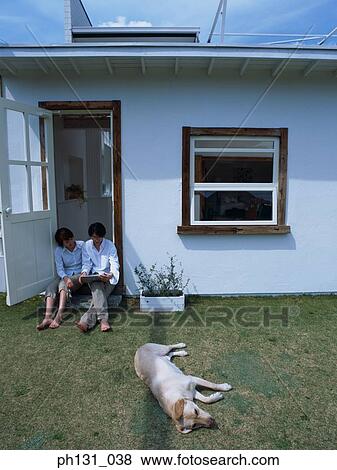 Stock Photo - Asian couple sitting at the door with their dog. Fotosearch