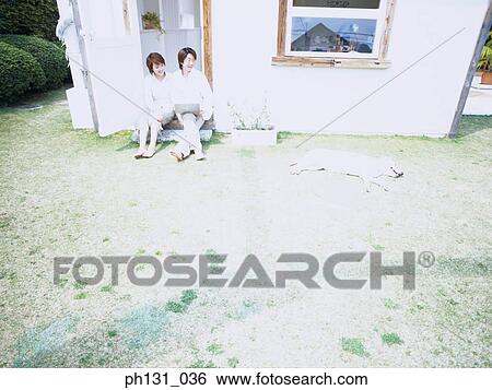 Stock Photograph - Asian couple sitting at the door with their dog. Fotosearch
