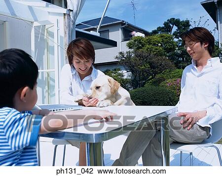 Stock Image - Asian family sitting out with their pet. Fotosearch