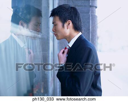 Stock Image - Asian Man checking his tie in a window. Fotosearch