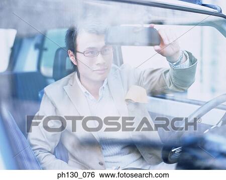 Stock Photograph - Asian Man looking at himself in the rearview mirror. Fotosearch