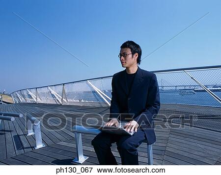 Stock Photo - Asian Man on a pier working on his laptop. Fotosearch