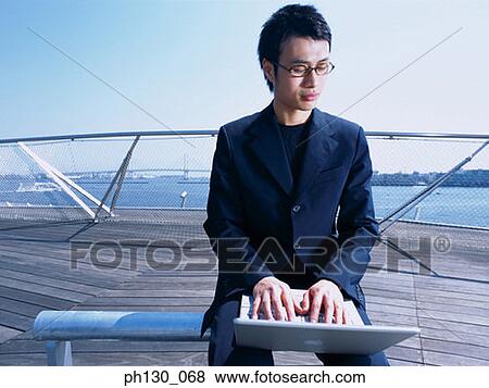 Stock Photo - Asian Man on a pier working on his laptop. Fotosearch