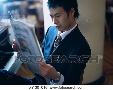 Stock Photograph - Asian Man reading the papers by a piano. Fotosearch