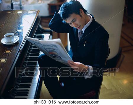 Stock Photography - Asian Man reading the papers by a piano. Fotosearch