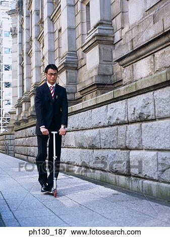 Asian Man riding a foot propelled scooter View Large Photo Image Stock Photo - Asian Man riding a foot propelled scooter. Fotosearch