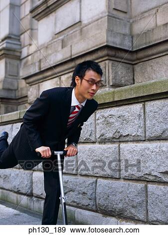 Asian Man riding a foot propelled scooter View Large Photo Image Stock Photo - Asian Man riding a foot propelled scooter. Fotosearch