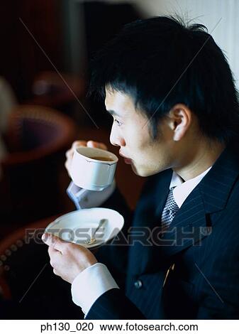 Stock Image - Asian Man sipping tea at a café. Fotosearch