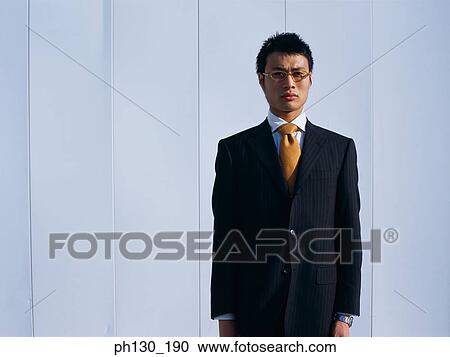 Stock Image - Asian Man standing in front of a wall. Fotosearch