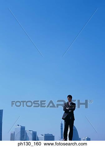 Stock Image - Asian Man standing in front of skyscrapers. Fotosearch