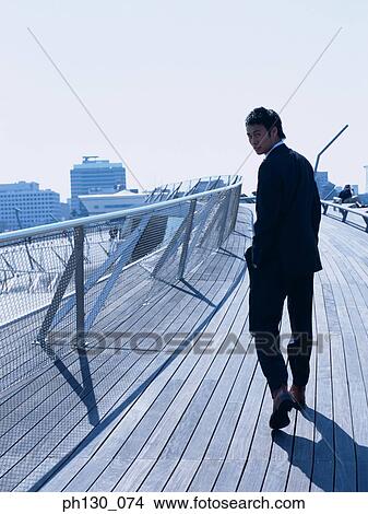 Picture - Asian Man walking on a bridge. Fotosearch