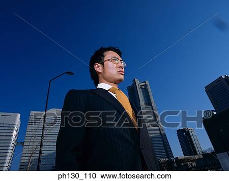Stock Image - Asian Standing amidst skyscrapers. Fotosearch