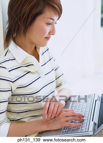 Stock Photo - Asian Woman working on a laptop. Fotosearch