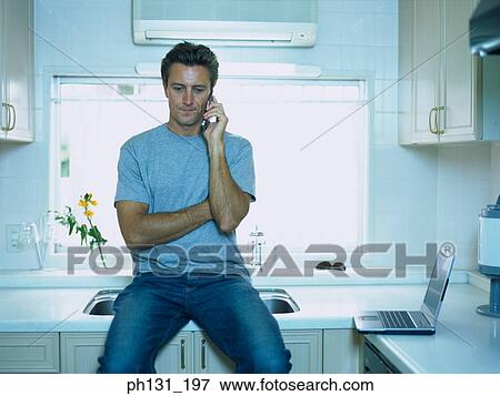 Man sitting on a basin counter with a cell phone View Large Photo Image Stock Photo - Man sitting on a basin counter with a cell phone. Fotosearch