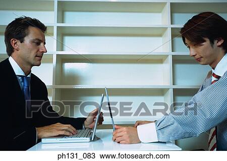 Stock Image - Two men with laptops at a meeting. Fotosearch