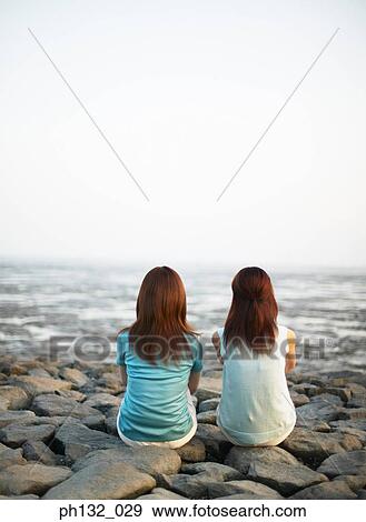 Two young women sitting by the shore View Large Photo Image Stock Photo - Two young women sitting by the shore. Fotosearch