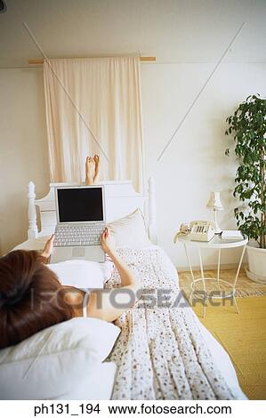 Picture - Woman lying on a bed with a laptop. Fotosearch