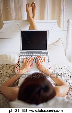 Woman lying on a bed with a laptop View Large Photo Image Stock Photography - Woman lying on a bed with a laptop. Fotosearch