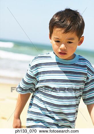 Stock Image - Young boy at the beach looking down. Fotosearch